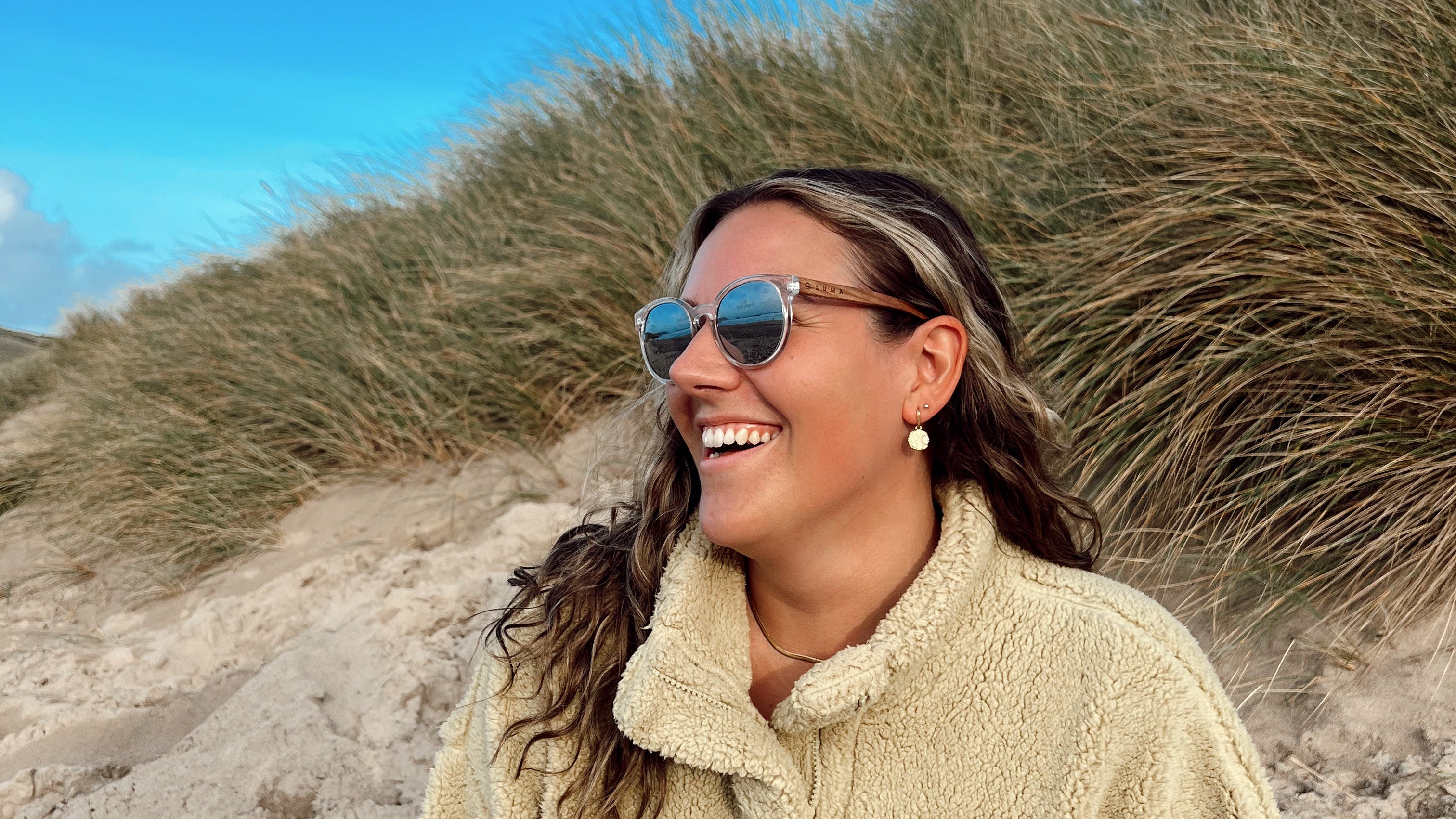WOMEN smiling sat on a beach wearing luma tarka sunglasses