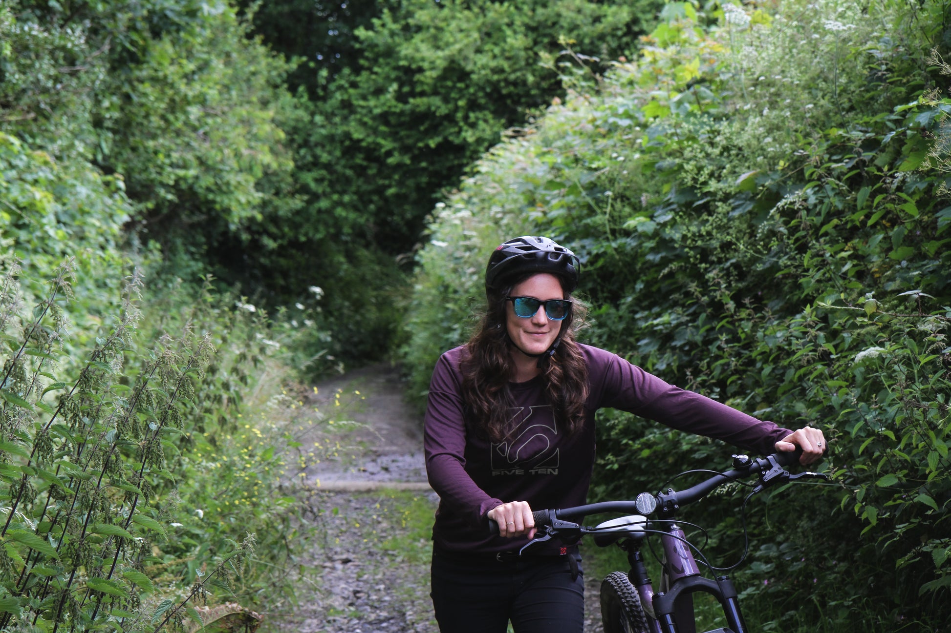 Women smiling outdoors wearing sunglasses while pushing mountain bike