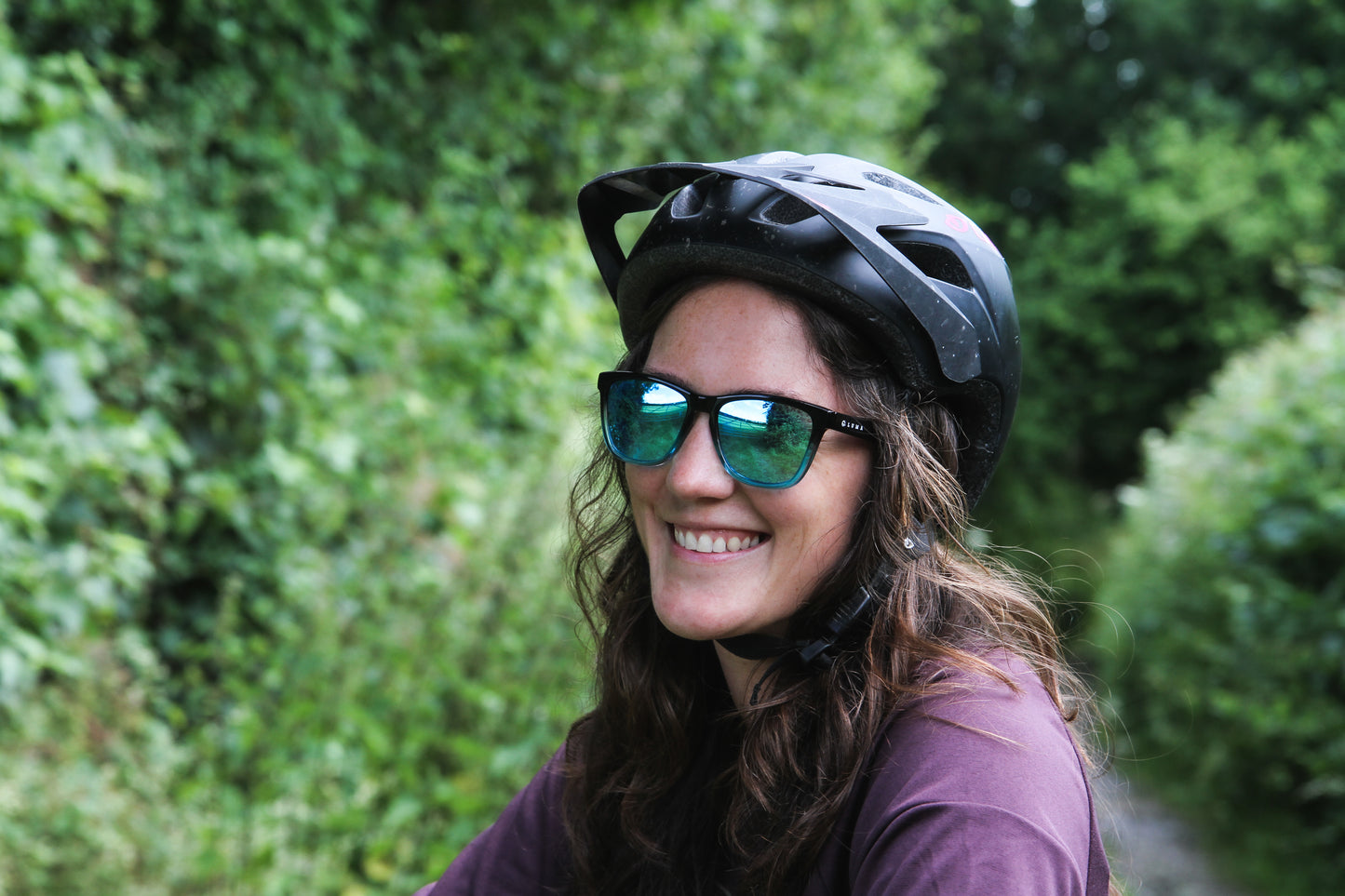 Women smiling outdoors wearing sunglasses and mountain bike helmet