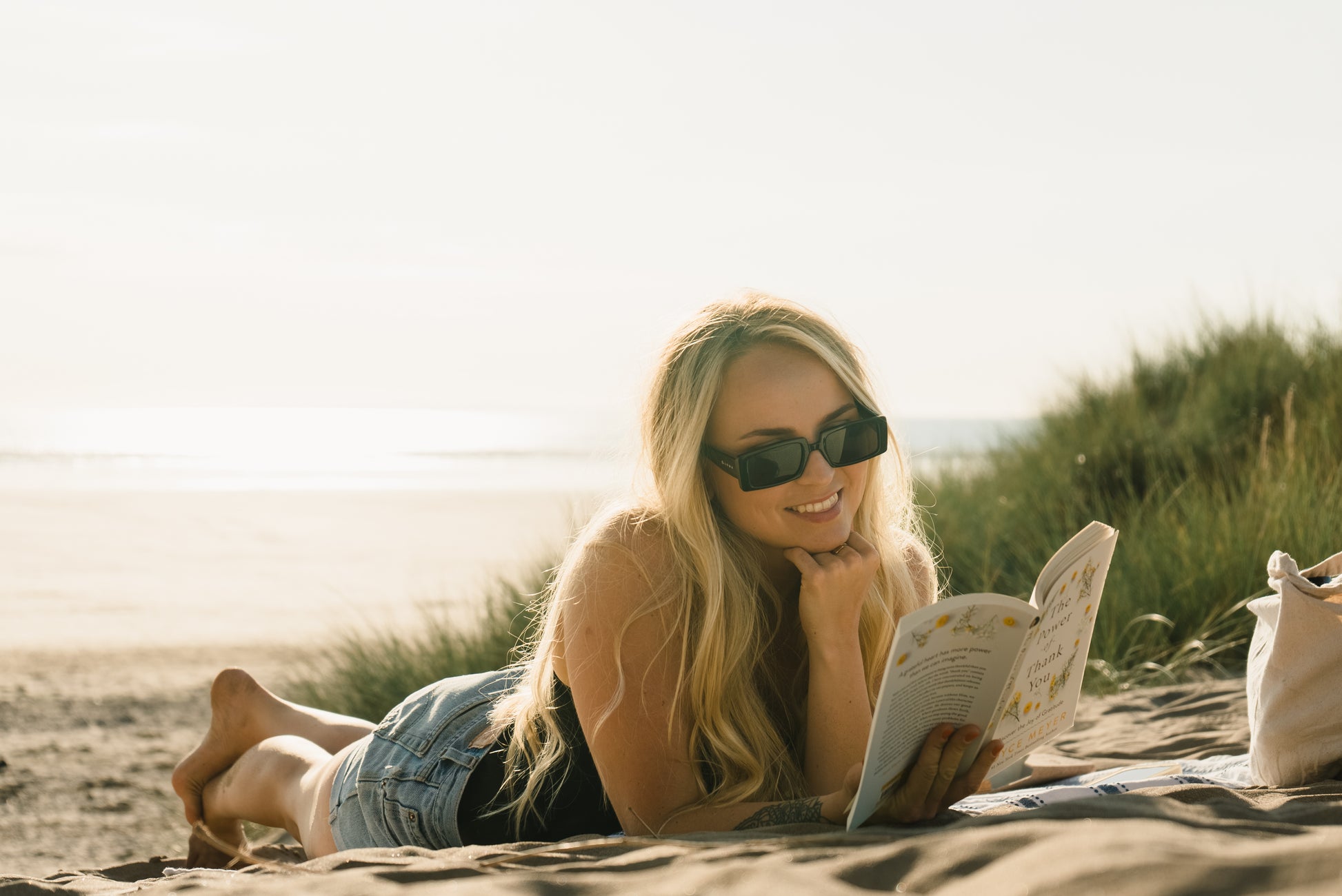 smiling women reading book on beach and wearing sunglasses